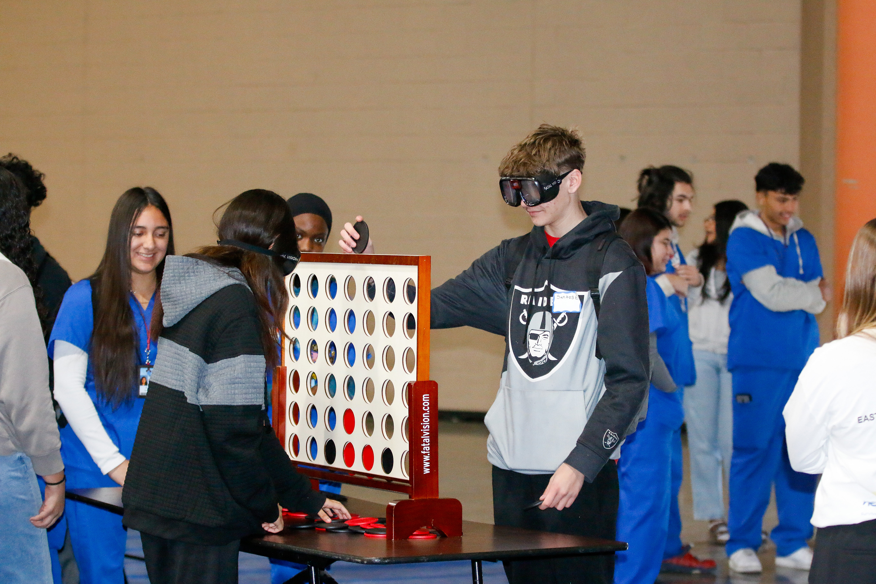 Students attempt to put a round disc into a board while wearing drunk goggles