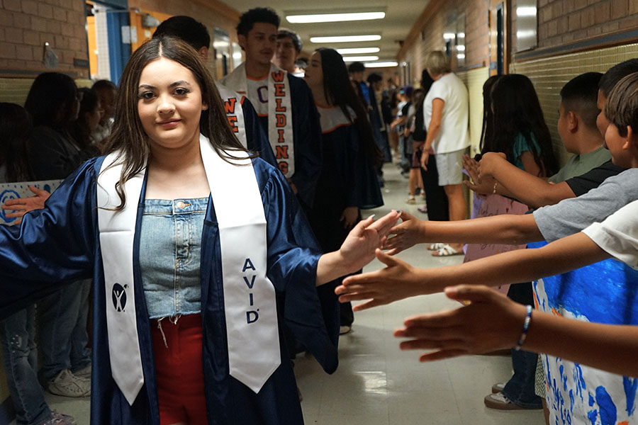 Students in graduation gowns give younger students high fives in the hallway