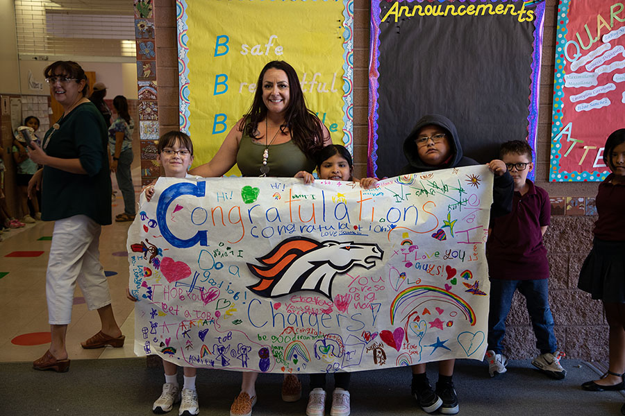 Students and a woman hold up a congratulations banner to welcome Cholla seniors
