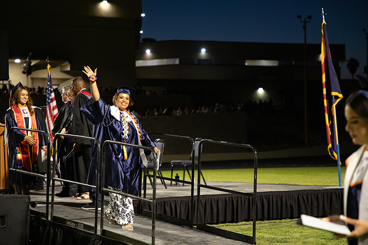 A graduate smiles and waves to her family as she walks off the stage