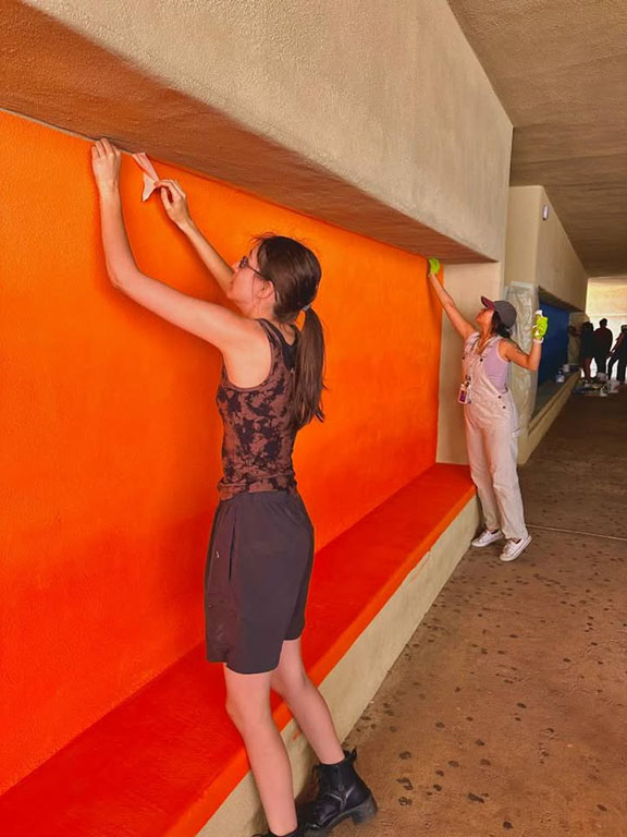 Students remove tape from a newly orange-painted wall at the school