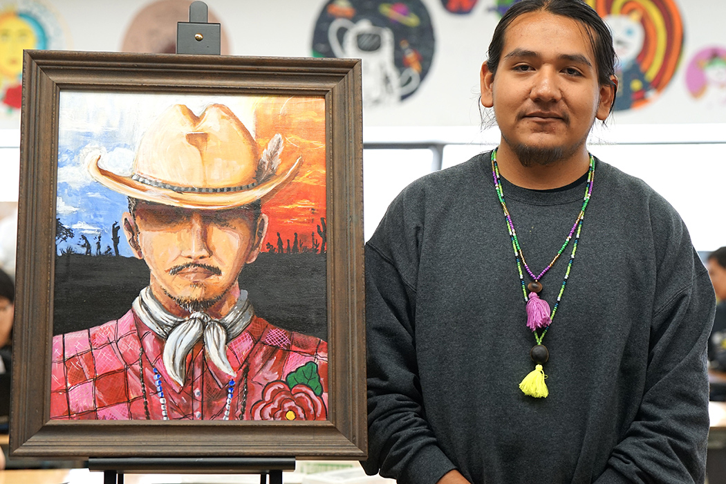 A teen boy wearing tribal necklaces shows off his artwork