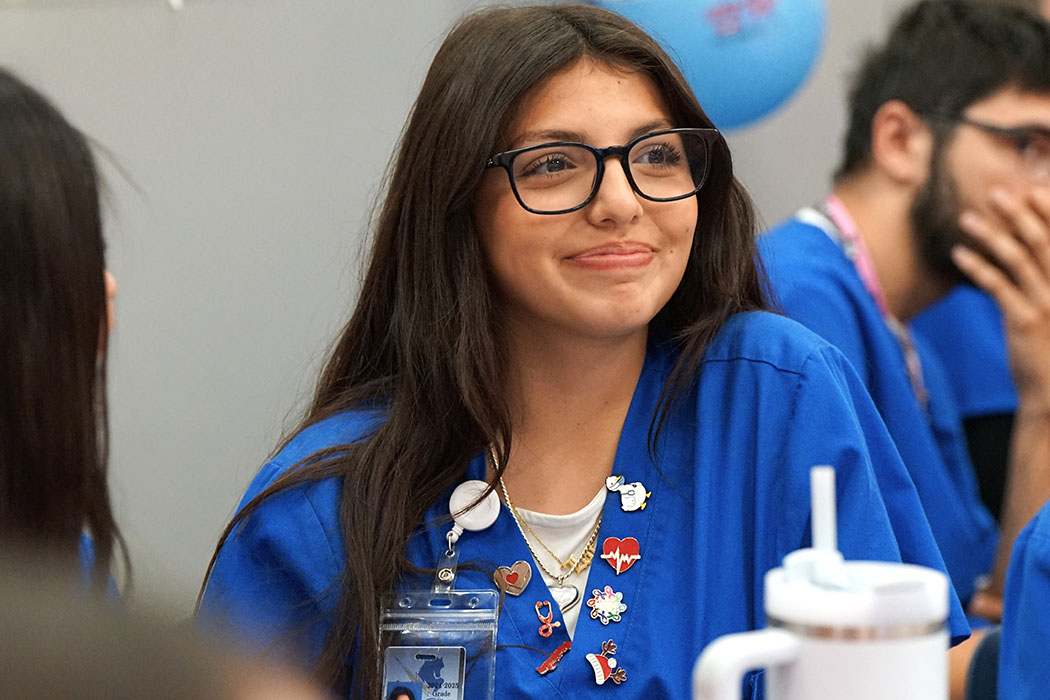 A girl in blue scrubs and glasses smiles