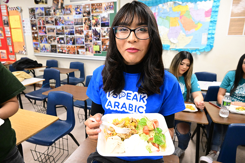 A teen girl with dark hair and glasses shows off her plate of Arabic food