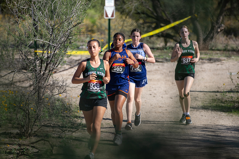 A group of teen girls run on a dirt trail