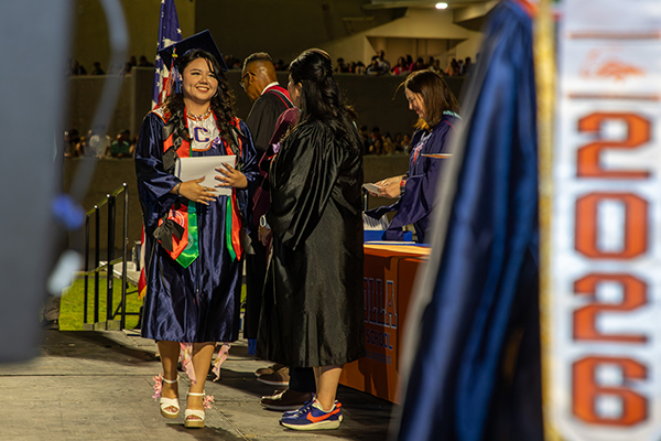 A teen girl graduate smiles as she gets her diploma