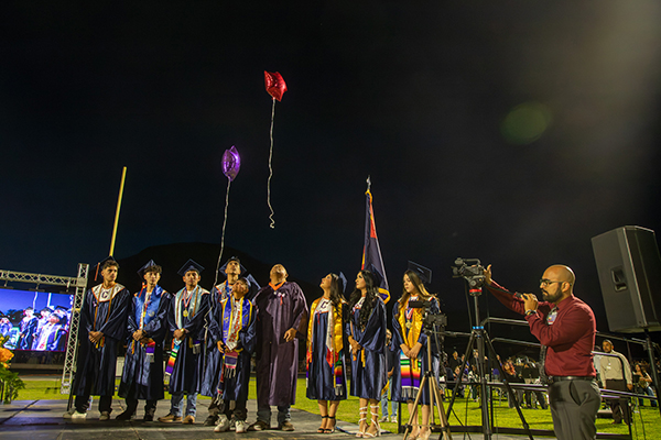 Graduates stand on the field watching balloons float up to the sky