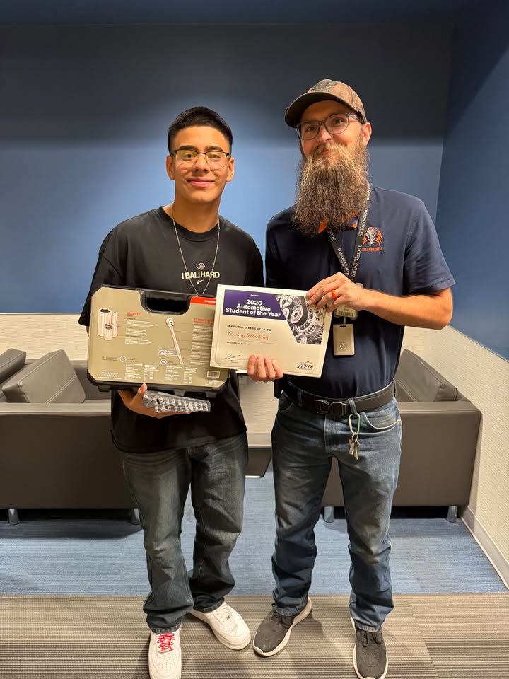 A teen boy holds up a plaque with his auto tech instructor