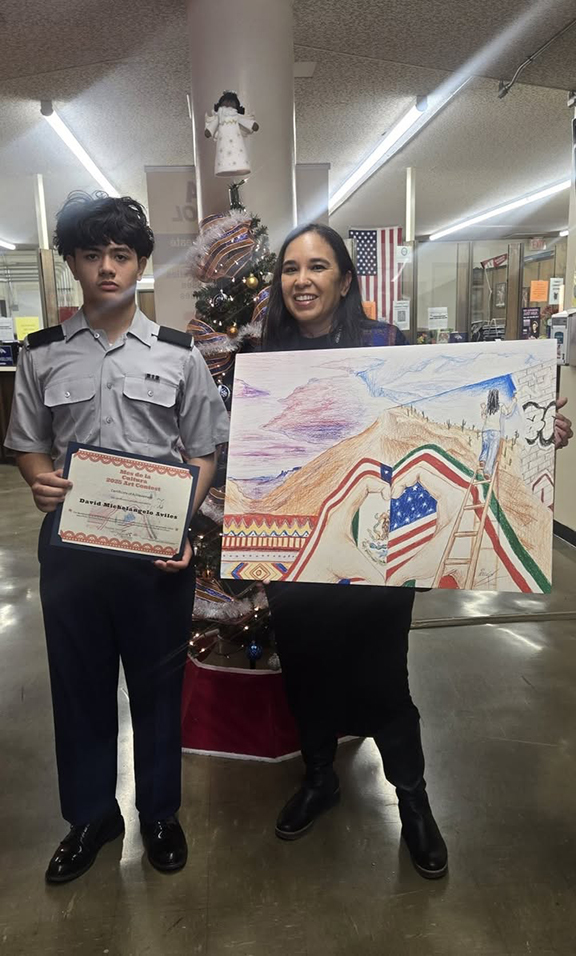 A teen boy holds up his award certificate, next to a woman holding his winning artwork