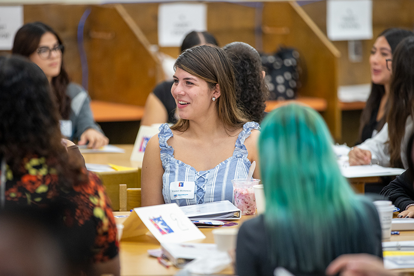 A woman animatedly talks to teen girls at her table
