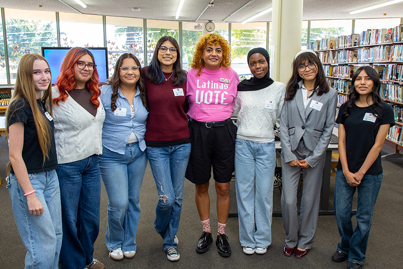 A group of teen girls smile for a photo with a woman in a pink Latinas Vote shirt