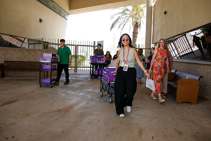 A woman smiles as she pulls a wagon full of purple boxes, with several people behind her pushing carts with purple boxes