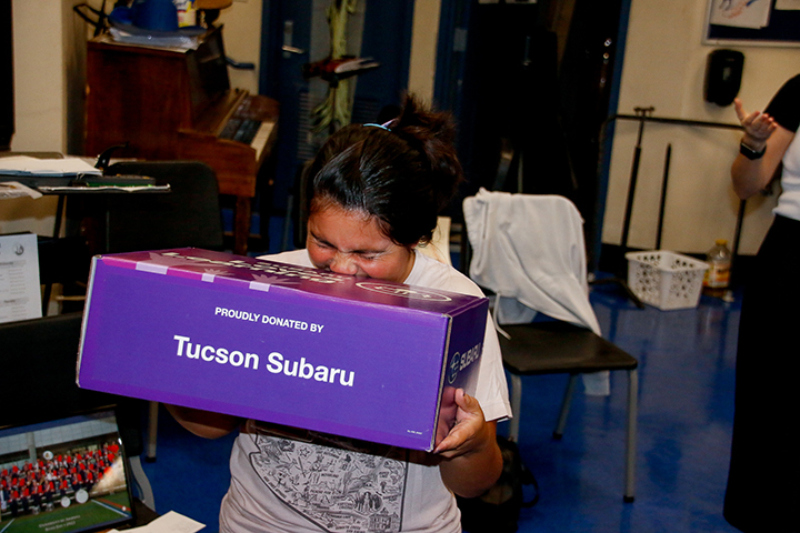 A woman excitedly holds a purple box with the words Proudly Donated by Tucson Subaru