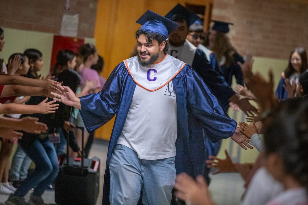A Cholla grad in his cap and gown gives out high fives to elementary students