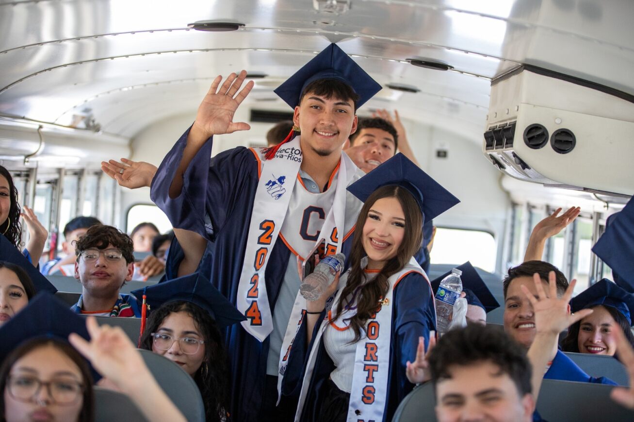 Cholla grads smile in their caps and gowns on the school bus