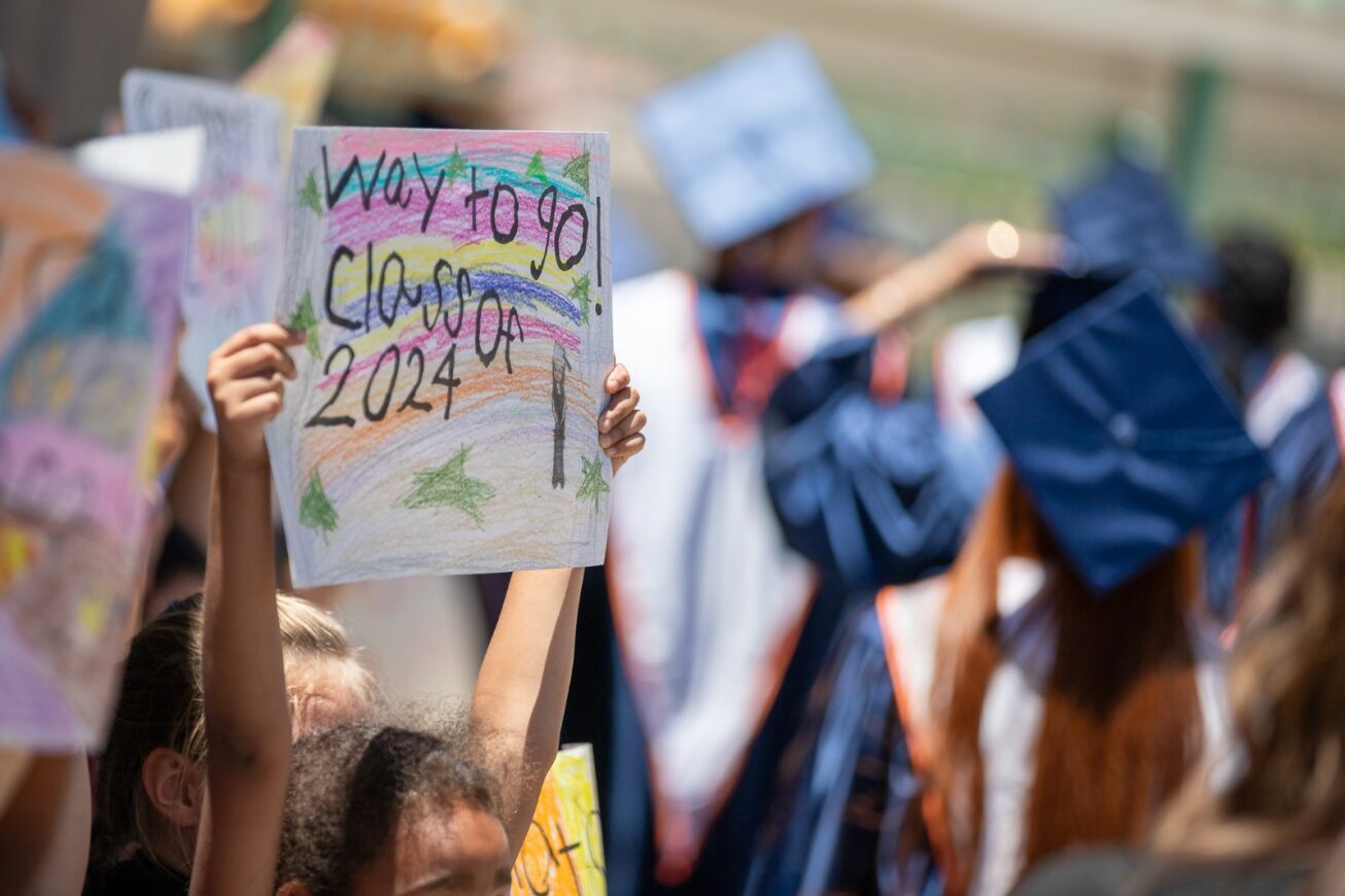 An elementary student holds up a sign reading Way to go class of 2024 for the grad parade