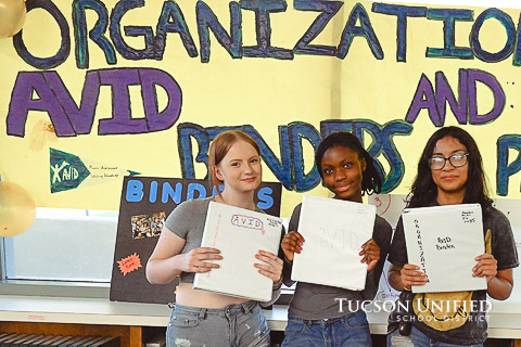 Student show off AVID binders while standing in front of a hand-made AVID sign.