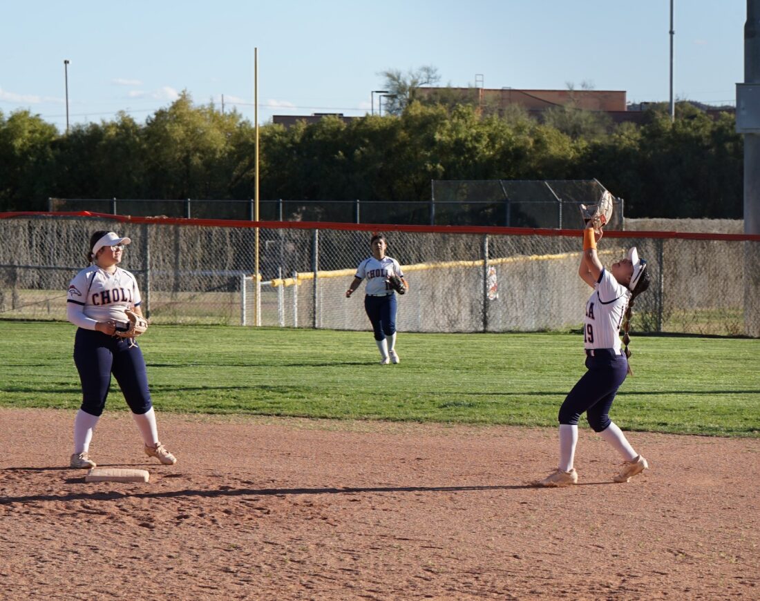 Cholla softball players in the outfield have their gloves out to catch the ball